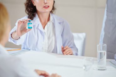 Female scientist showing vial with covid-19 vaccines to her colleagues and medical conference