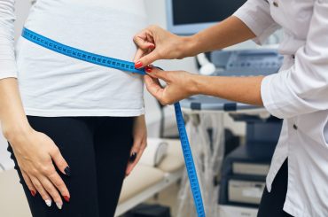 therapist is measuring a stomack of a woman who carries a baby, close up cropped side view photo.
